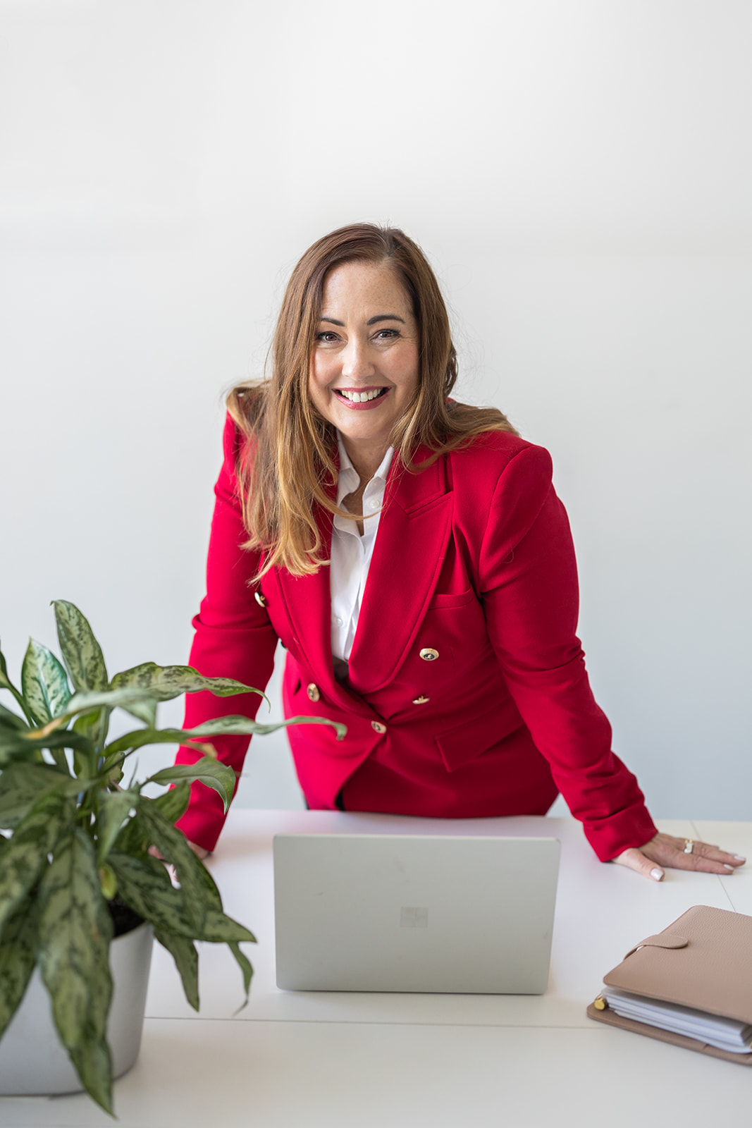 Helen Walsh smiling at her desk in a red blazer